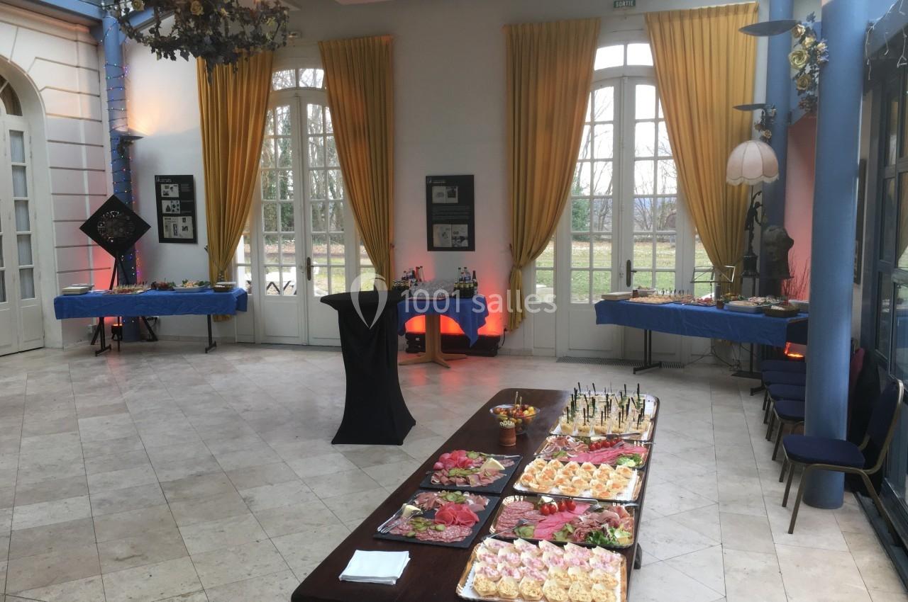 Salle lumineuse avec grandes fenêtres, tables dressées pour un buffet, plats variés disposés sur une table centrale.