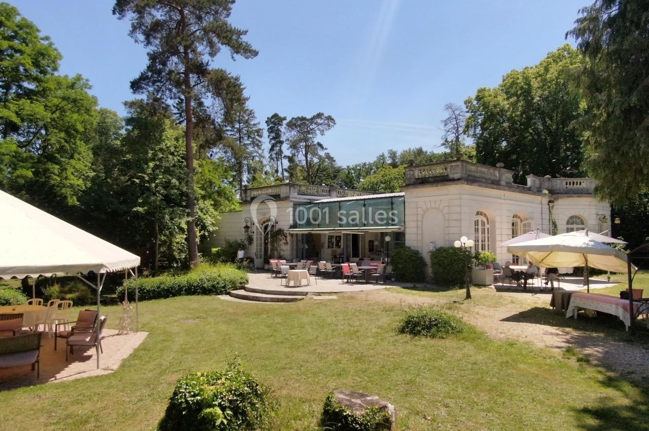 Bâtiment ancien entouré de verdure avec une terrasse aménagée et des tentes installées dans un jardin.