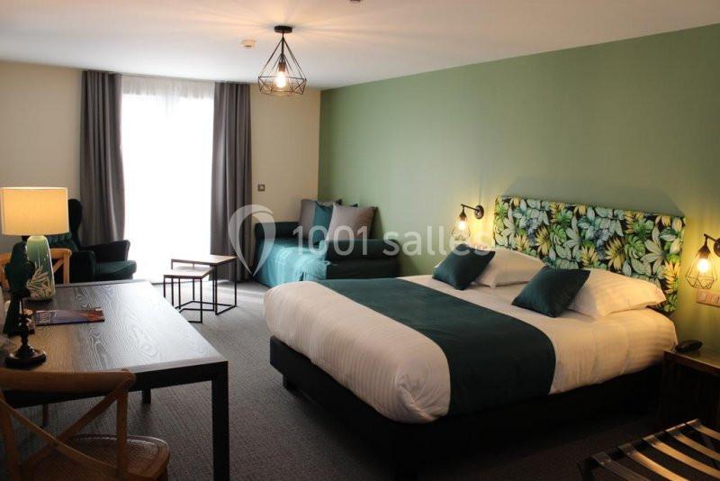 Chambre d'hôtel lumineuse avec un lit double, un canapé, un bureau en bois et une décoration aux tons verts.