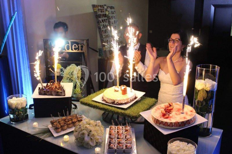 Un couple célèbre un événement devant une table garnie de desserts décorés de cierges magiques.
