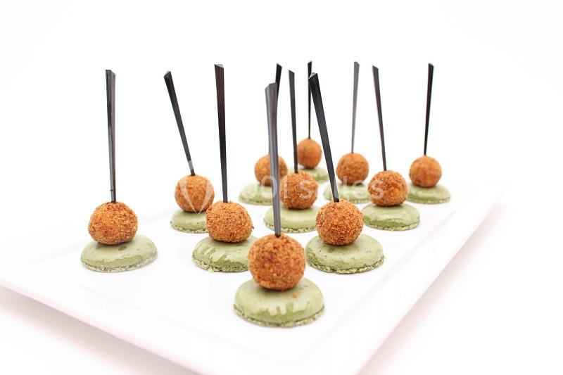 Bouchées apéritives composées de macarons verts et de billes panées surmontées de piques noires, présentées sur un plateau…