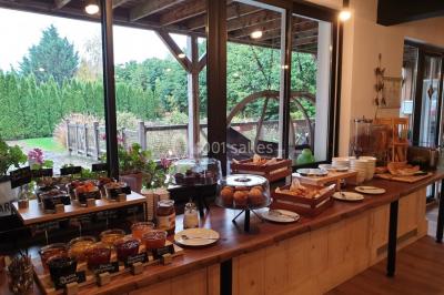Buffet de petit-déjeuner avec viennoiseries, confitures, pains et boissons, près d'une baie vitrée donnant sur un jardin.