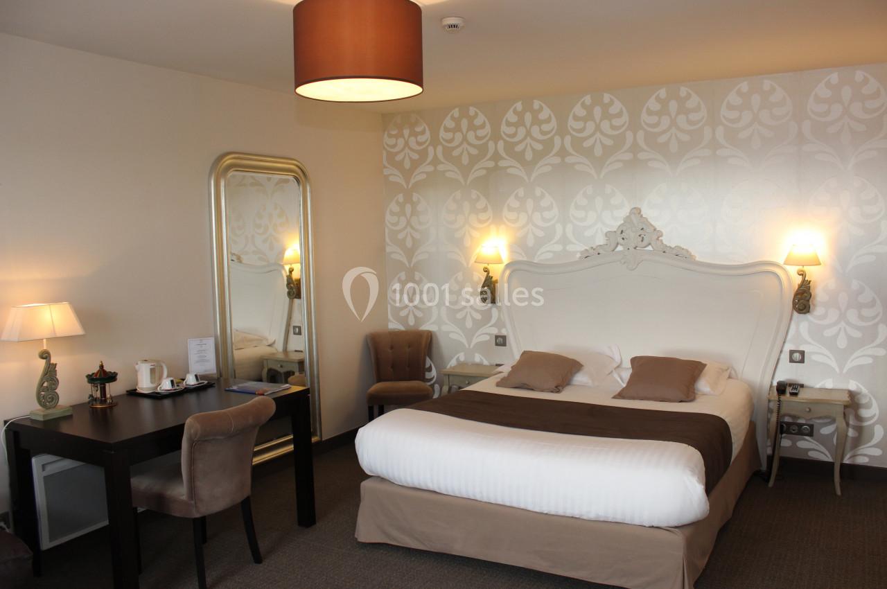 Chambre d'hôtel avec lit double, bureau, miroir, fauteuils et éclairage chaleureux dans une décoration élégante.