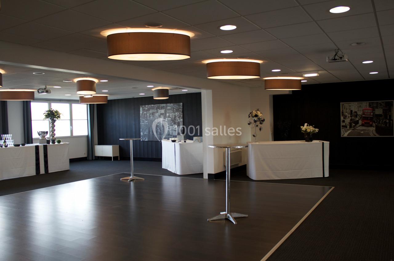 Salle de réception moderne avec parquet, tables hautes, décor sobre et éclairage suspendu.