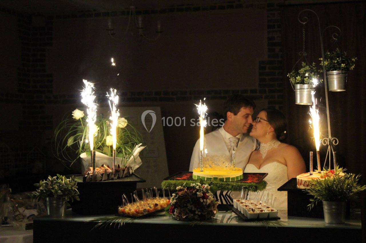 Un couple de mariés se tient près d'une table décorée avec des desserts et des fontaines lumineuses allumées.
