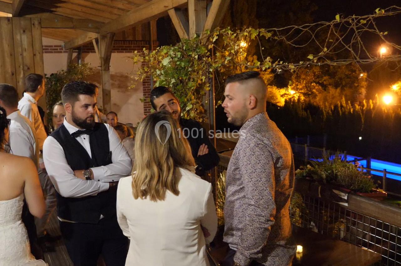 Groupe de personnes discutant sur une terrasse éclairée en soirée, avec une piscine visible en arrière-plan.