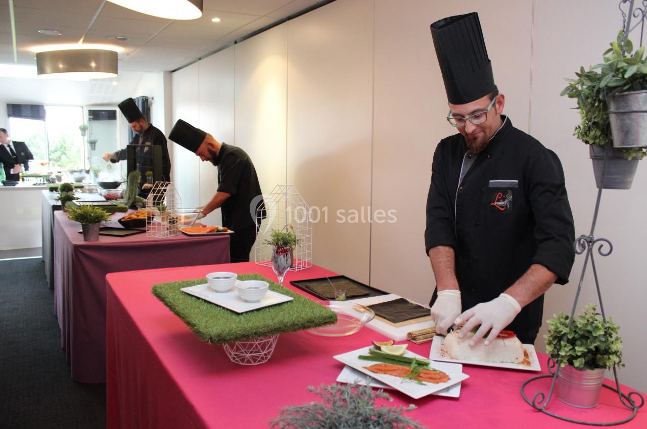 Des chefs en tenue préparent des plats sur des tables décorées dans une salle lumineuse.