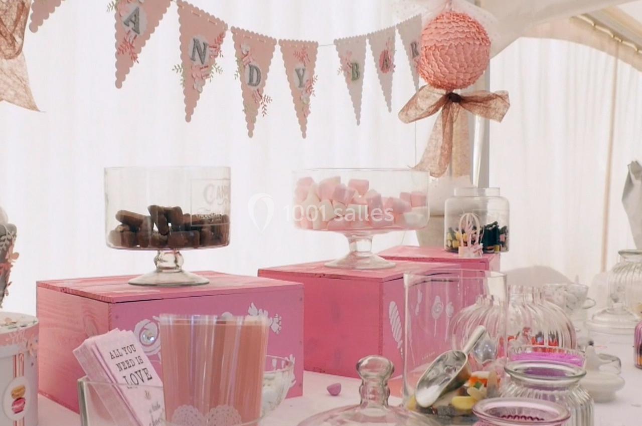 Table décorée avec des bonbonnières remplies de sucreries, des boîtes roses et une guirlande festive en arrière-plan.