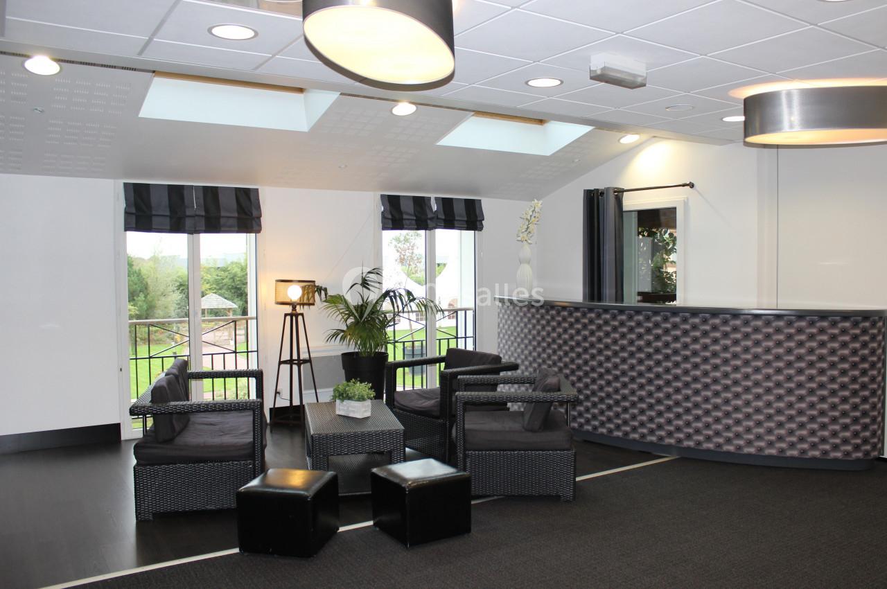 Espace d'accueil moderne avec comptoir, fauteuils en rotin, lampadaire et vue sur un jardin à travers des fenêtres.