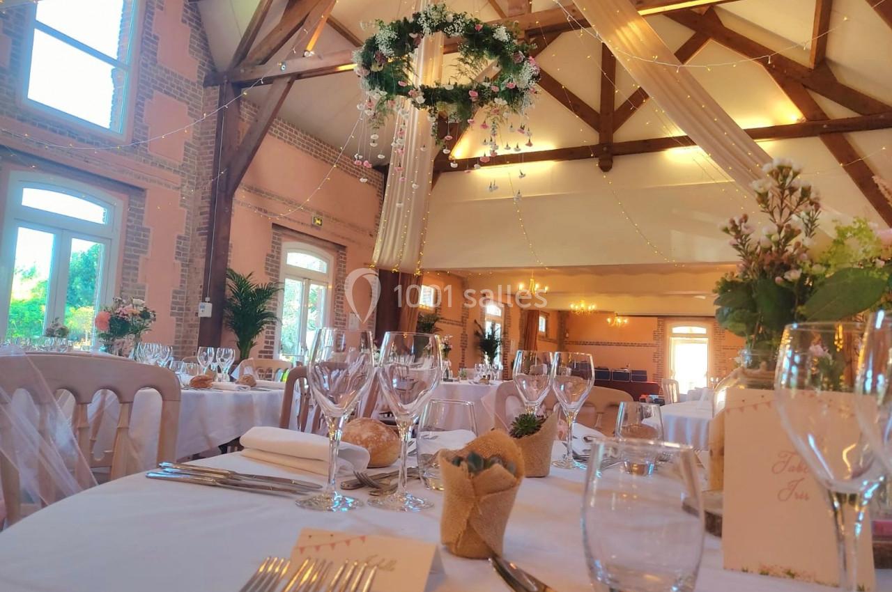Salle de réception décorée avec des tables dressées, des guirlandes lumineuses et une suspension florale centrale.