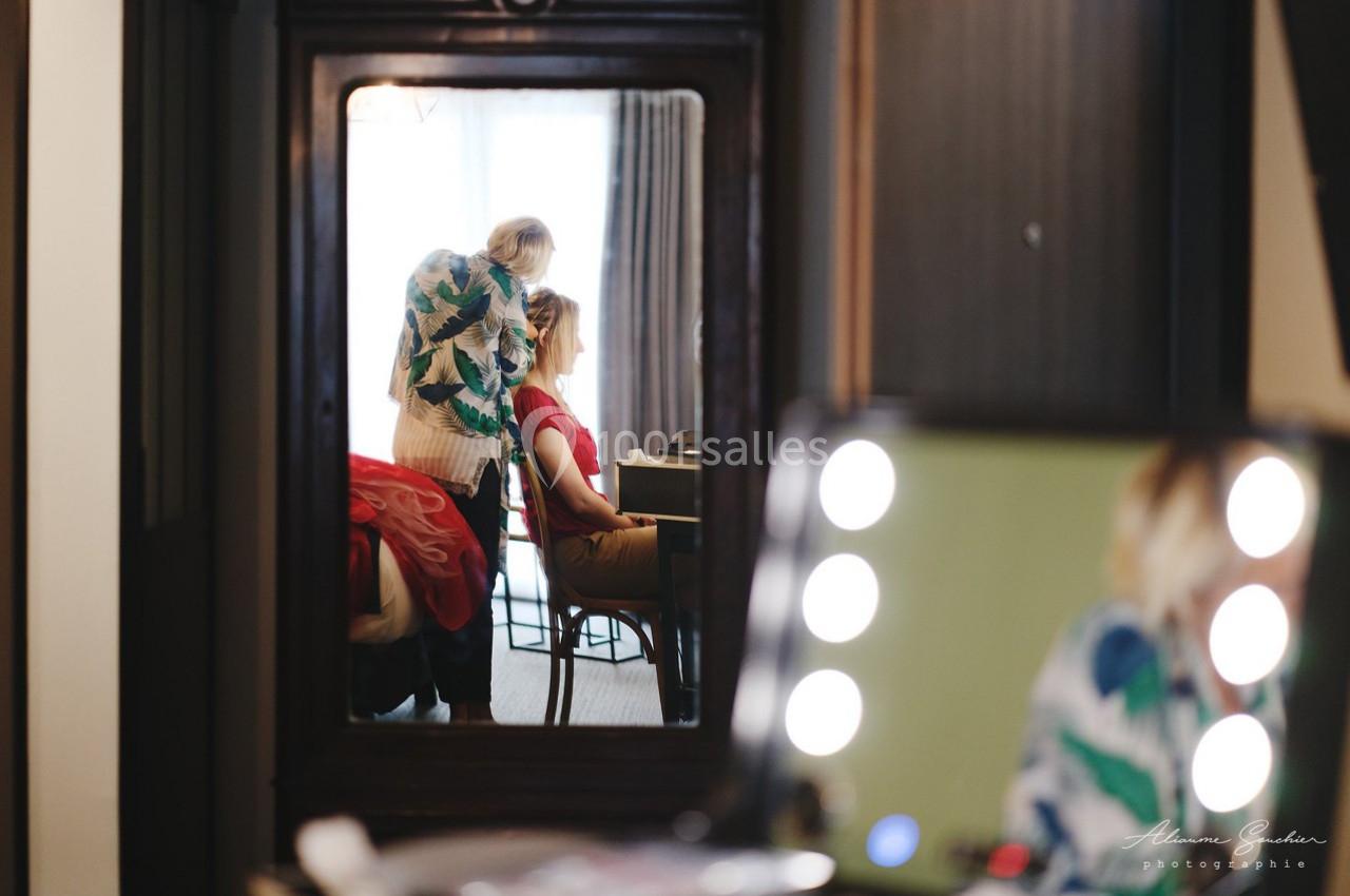 Une coiffeuse ajuste la coiffure d'une femme assise, reflétées dans un miroir ancien.