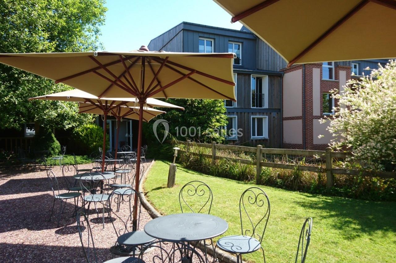 Terrasse extérieure avec tables en métal et parasols, entourée de verdure et de bâtiments résidentiels.