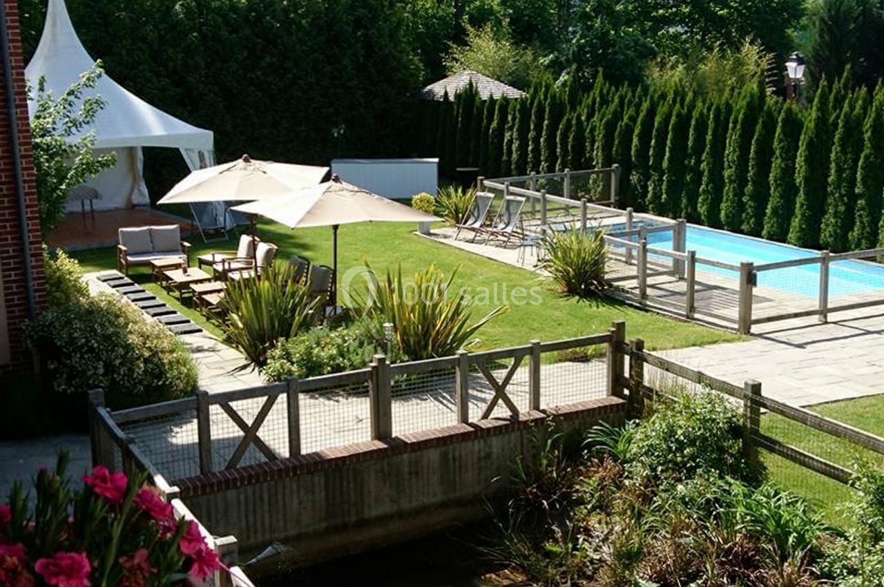 Jardin aménagé avec piscine, terrasse, parasols, mobilier d'extérieur et haies de conifères en arrière-plan.