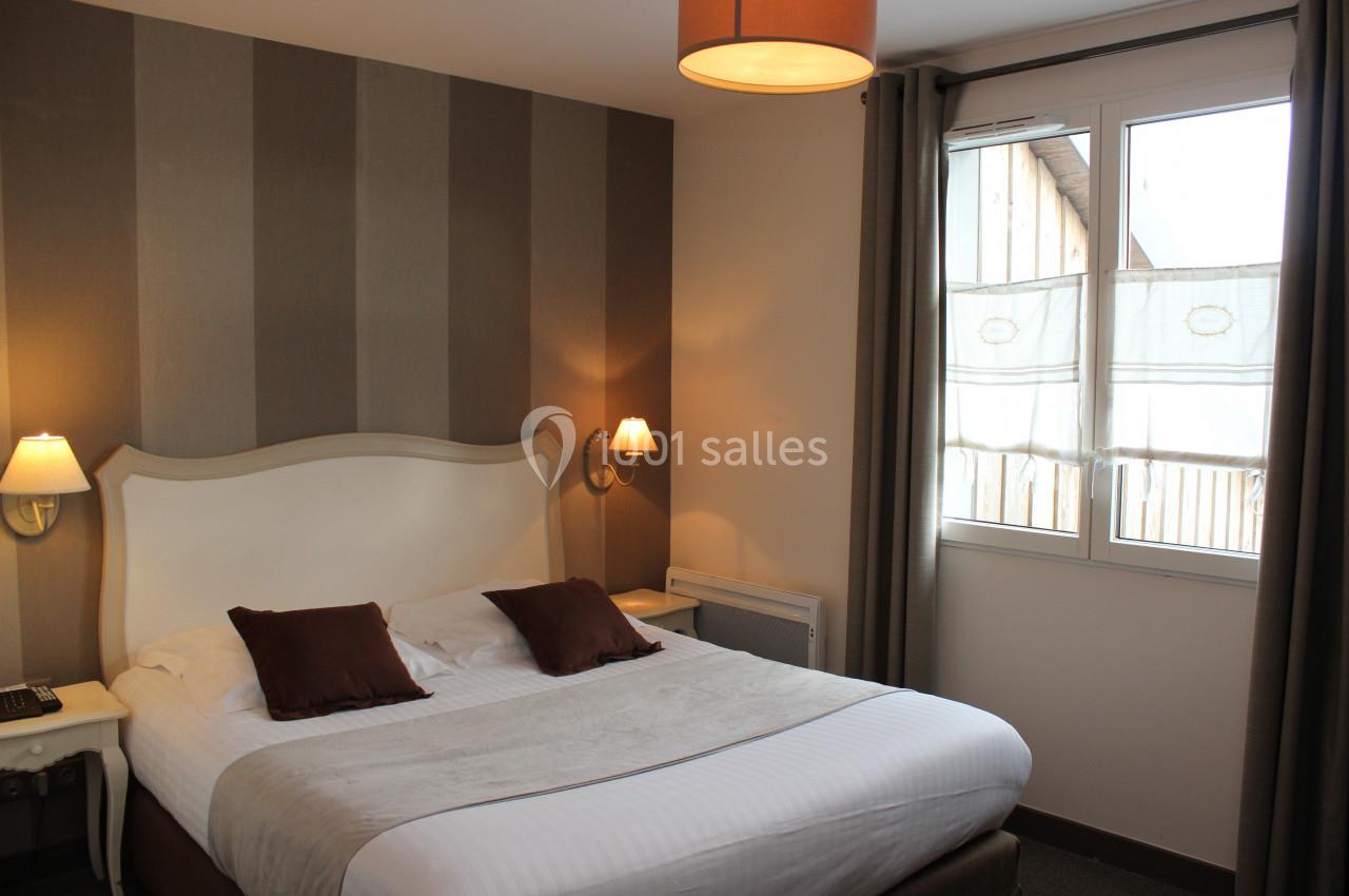 Chambre avec lit double, murs à rayures, deux lampes murales et une fenêtre avec rideaux donnant sur l'extérieur.