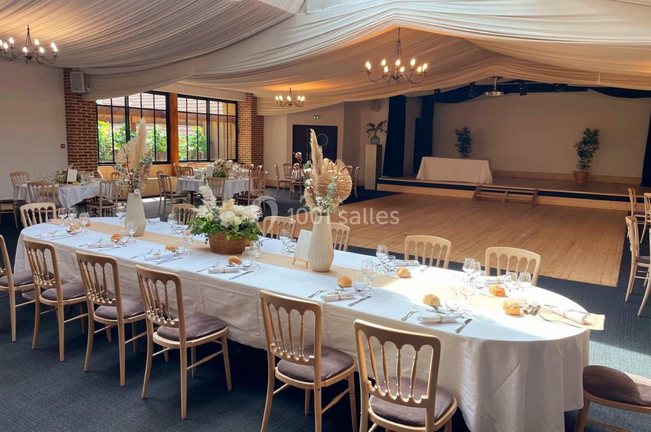 Salle de réception lumineuse avec tables dressées, chaises en bois clair et décorations florales élégantes.