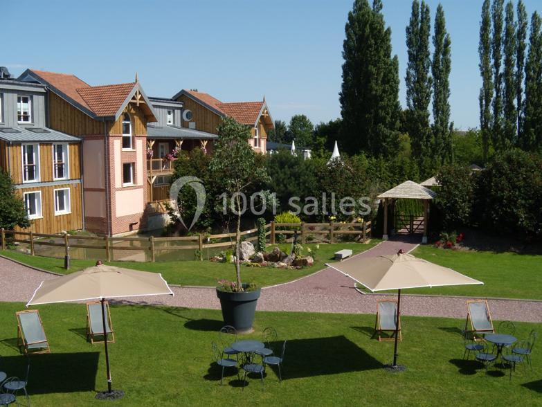 Jardin aménagé avec tables, chaises et parasols, entouré de bâtiments en bois et de végétation.