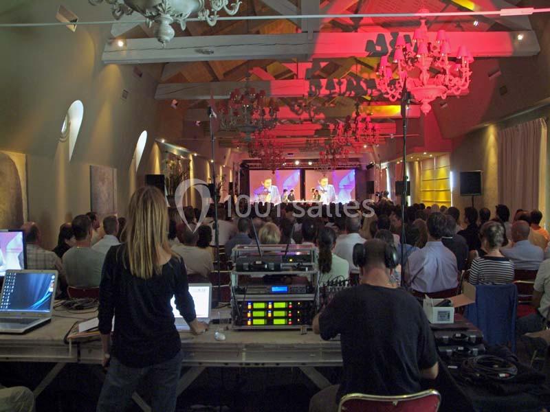 Un public assiste à un concert dans une salle éclairée, avec une régie technique visible au premier plan.