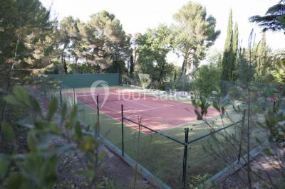 Terrain de tennis en plein air entouré de végétation et d'arbres, avec une clôture grillagée.