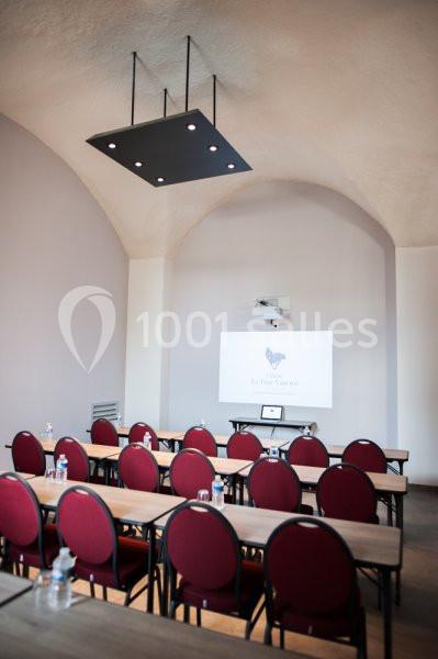 Salle de réunion avec des chaises rouges, des tables en bois, un projecteur et un écran blanc sous un plafond voûté.