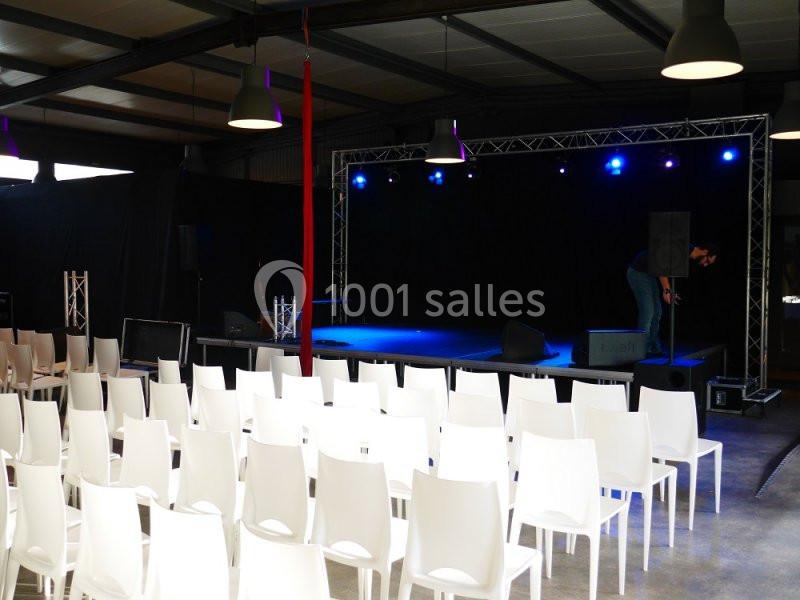 Salle avec des chaises blanches alignées face à une scène éclairée par des projecteurs bleus.