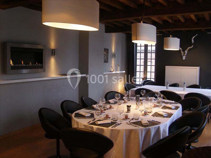 Salle de restaurant élégante avec table ronde dressée, chaises noires, cheminée moderne et éclairage suspendu.