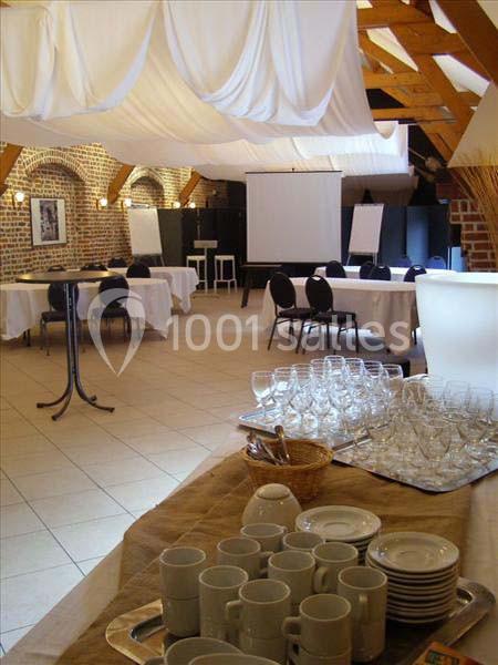 Salle de séminaire avec tables dressées, chaises, écran de projection et espace pour boissons et vaisselle.