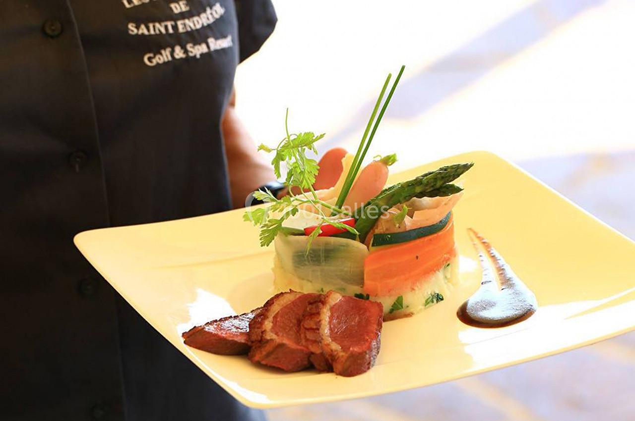 Assiette gastronomique avec viande, légumes dressés en rouleaux, asperges, purée et sauce, tenue par un serveur.