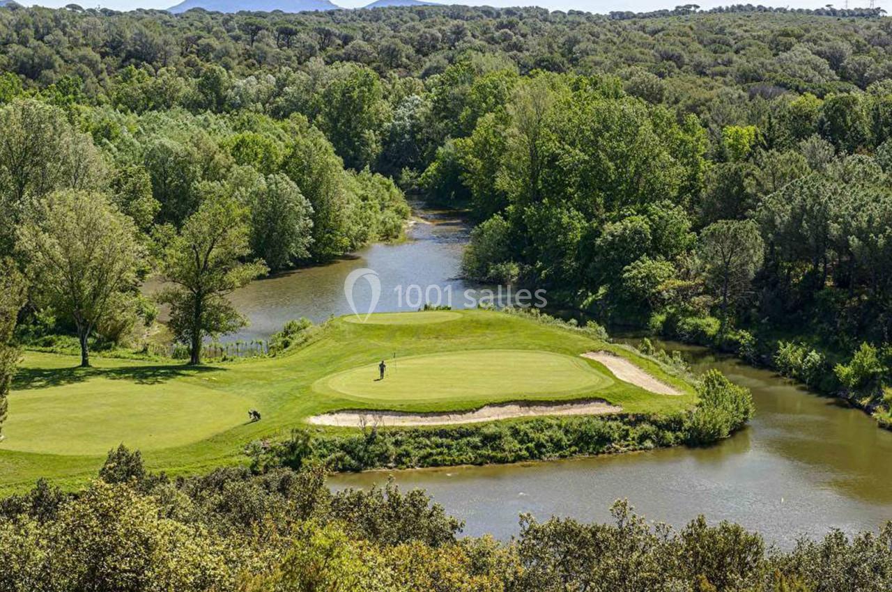 Vue d'un terrain de golf entouré d'arbres et bordé par une rivière dans un paysage naturel verdoyant.