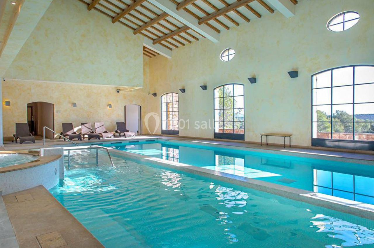 Piscine intérieure lumineuse avec grandes fenêtres, chaises longues et plafond en bois dans un cadre chaleureux.