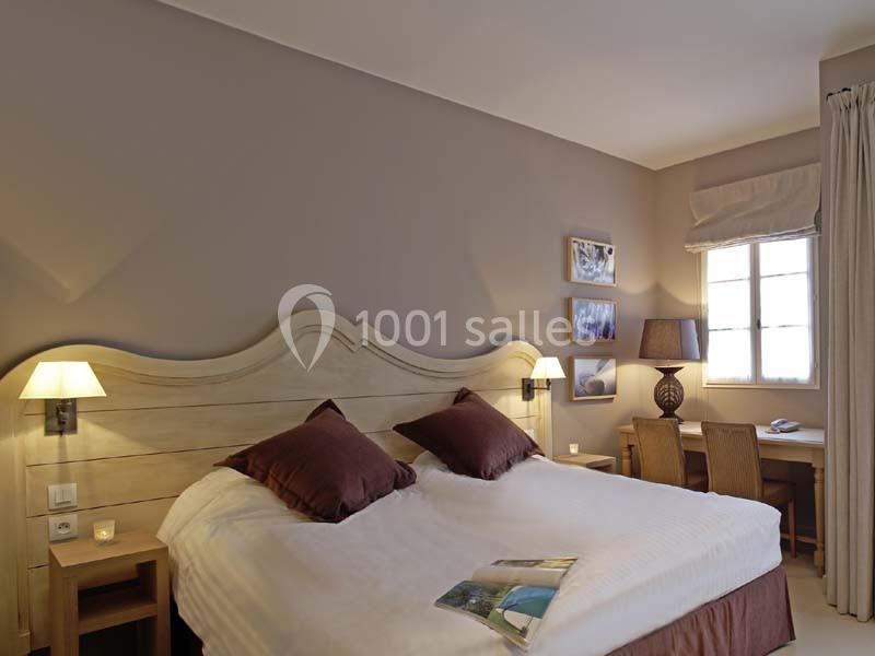 Chambre avec lit double, tête de lit en bois, lampes de chevet, bureau en bois et fenêtre avec rideaux beiges.