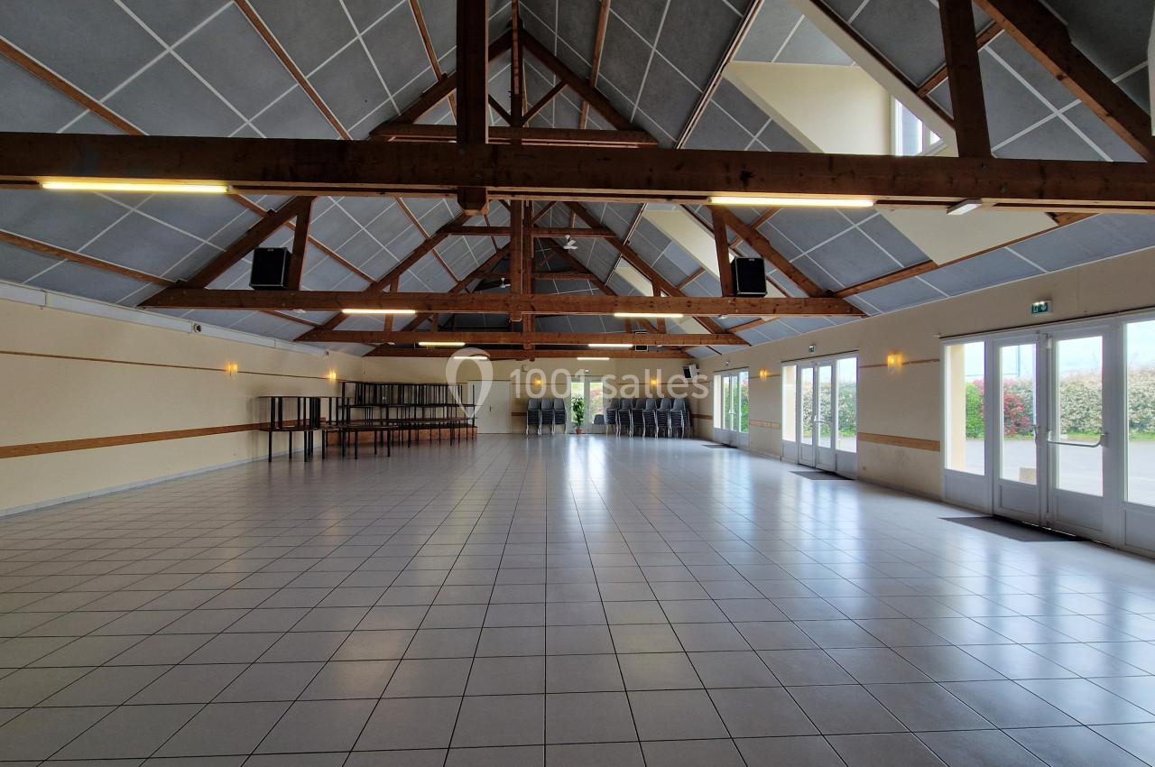 Grande salle lumineuse avec charpente en bois apparente, carrelage au sol et baies vitrées donnant sur l'extérieur.