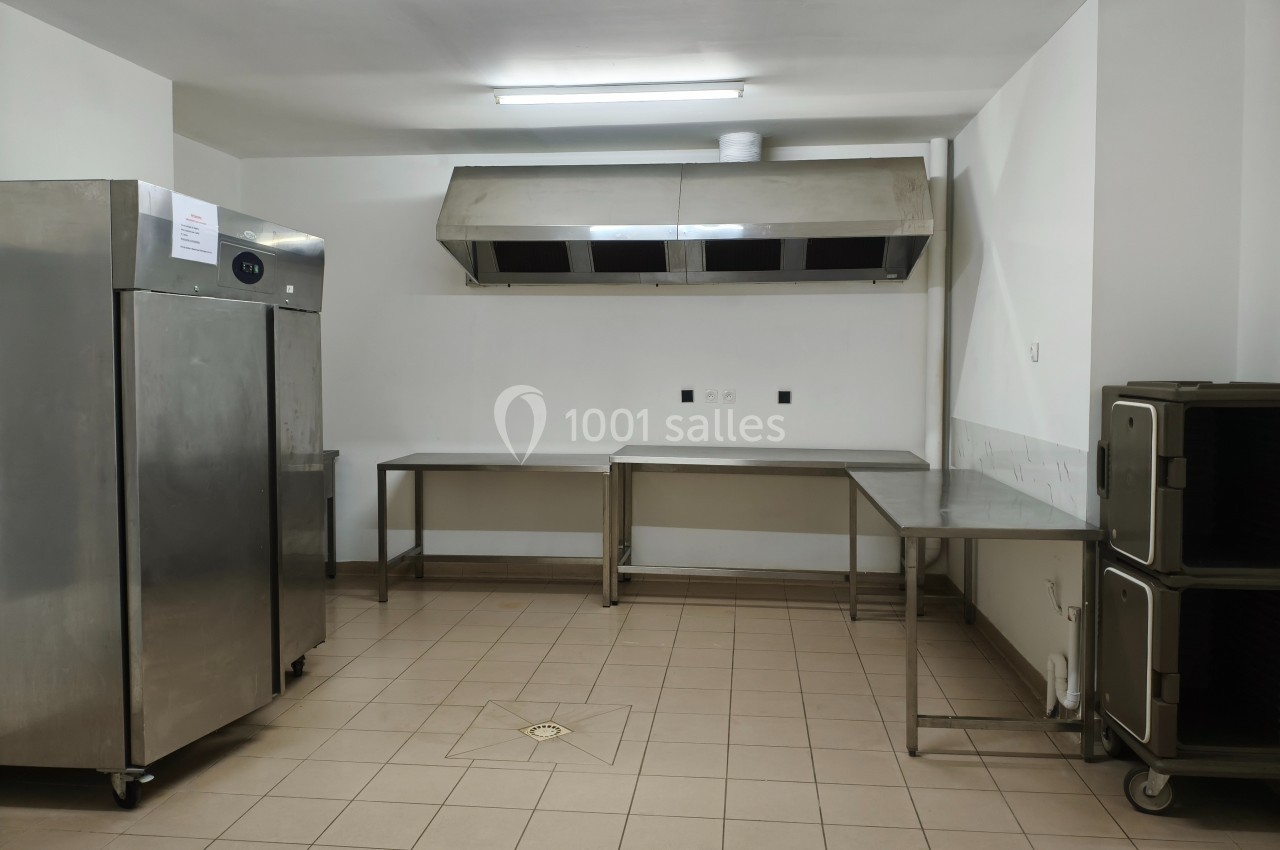 Cuisine professionnelle vide avec sol carrelé, plans de travail en inox, hotte aspirante et équipements de rangement.