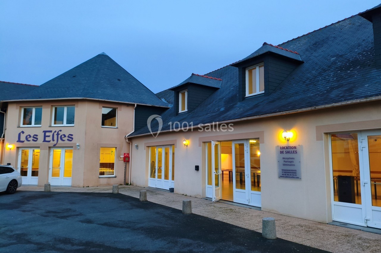 Façade d'un bâtiment avec des fenêtres éclairées, une enseigne ’Les Elfes’ et un panneau indiquant une location de salles.