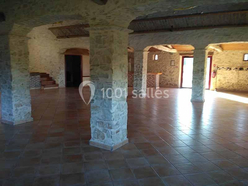 Salle spacieuse avec murs en pierre, colonnes, sol carrelé et lumière naturelle entrant par des ouvertures.