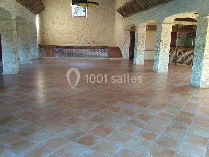 Salle vide avec sol en carrelage beige, murs en pierre apparente et plafond avec poutres en bois.