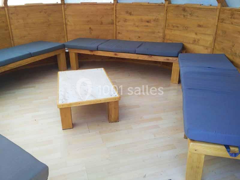 Bancs en bois avec coussins bleus disposés en cercle autour d'une table basse dans une pièce au sol en parquet clair.