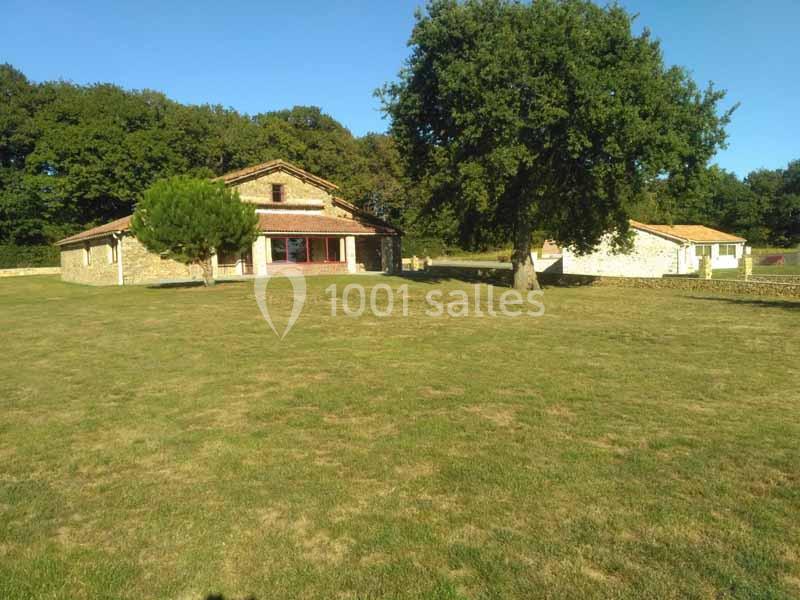 Maison en pierre entourée d'un grand jardin avec pelouse, arbres et ciel dégagé en arrière-plan.