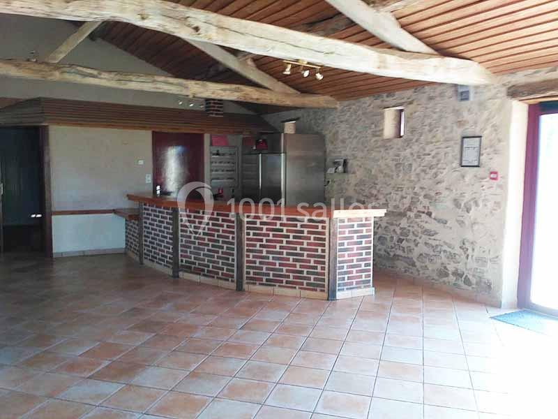 Salle avec un comptoir en briques, sol en carrelage, murs en pierre et poutres apparentes au plafond.