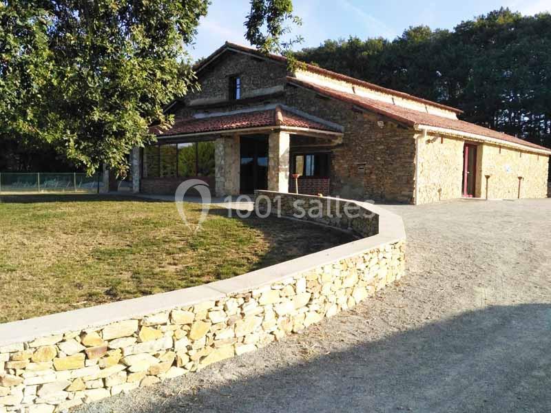Maison en pierre avec toit en tuiles rouges, entourée d'un muret en pierre et d'un espace vert, sous un ciel dégagé.