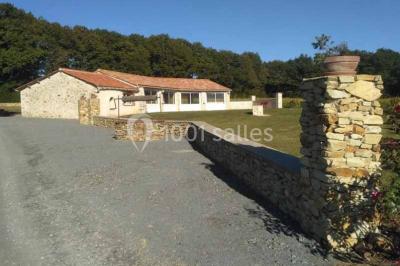 Chemin de gravier bordé de murets en pierre, menant à un paysage rural avec champs et arbres.