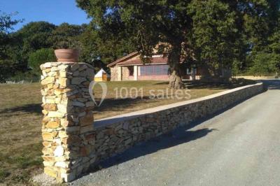 Chemin de gravier bordé de murets en pierre, menant à un paysage rural avec champs et arbres.