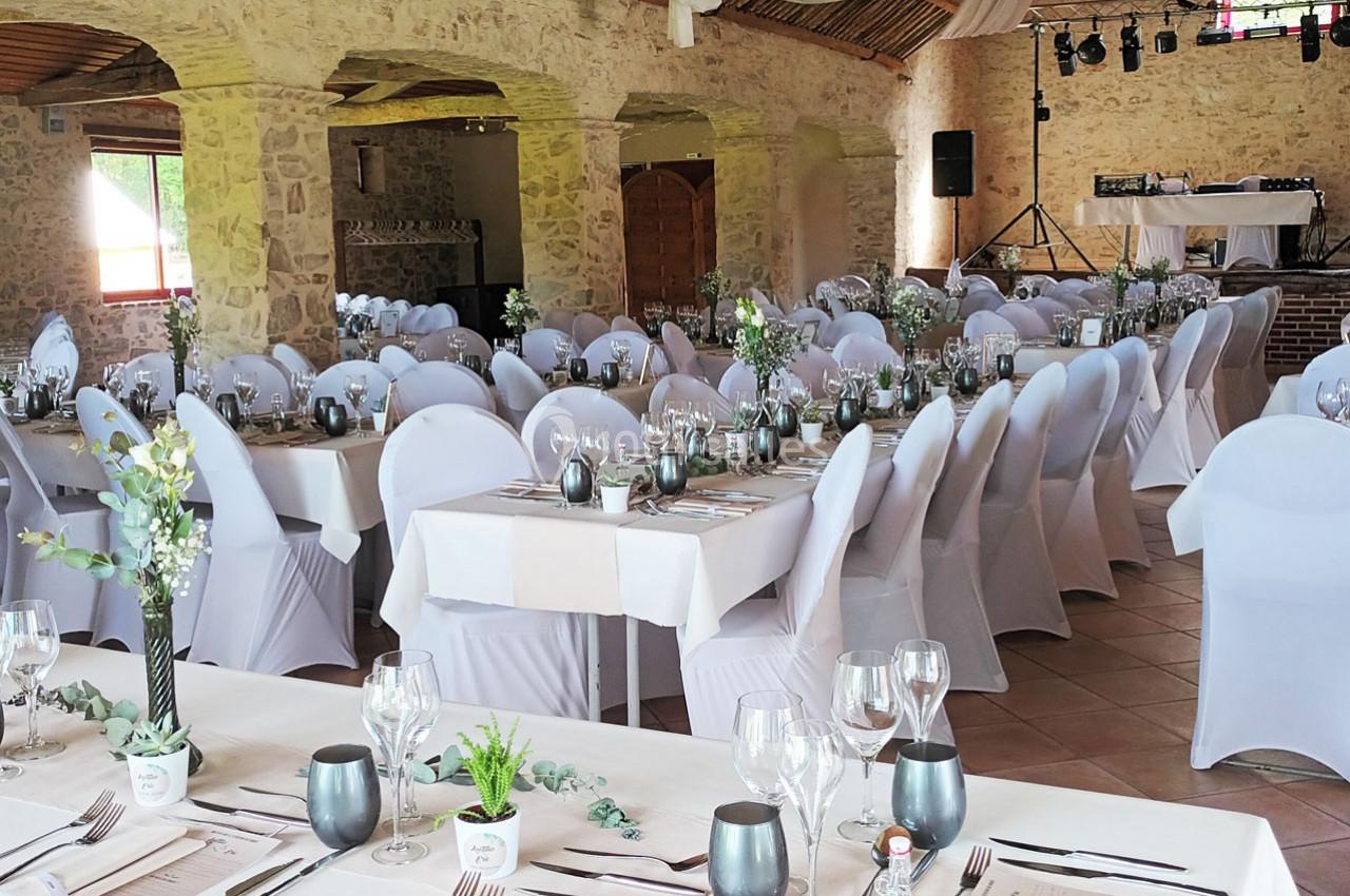 Salle de réception décorée pour un événement, avec des tables dressées, des chaises blanches et des arrangements floraux.