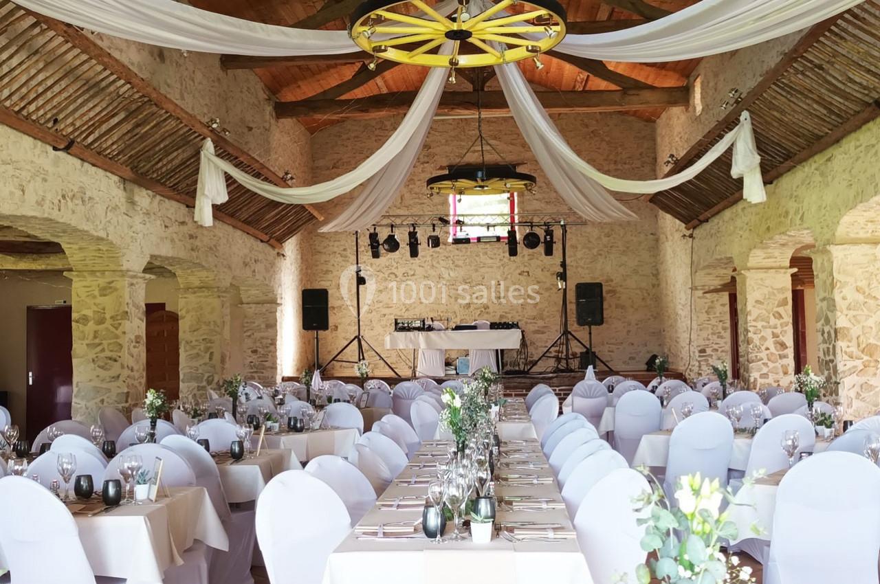 Salle de réception en pierre avec tables décorées, chaises blanches et drapés suspendus au plafond.