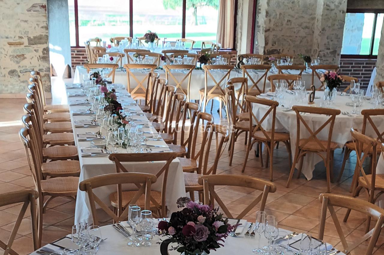 Salle de réception lumineuse avec tables dressées, chaises en bois et décorations florales.