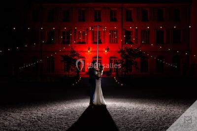 Un couple danse sous des guirlandes lumineuses devant un bâtiment éclairé en rouge, de nuit.