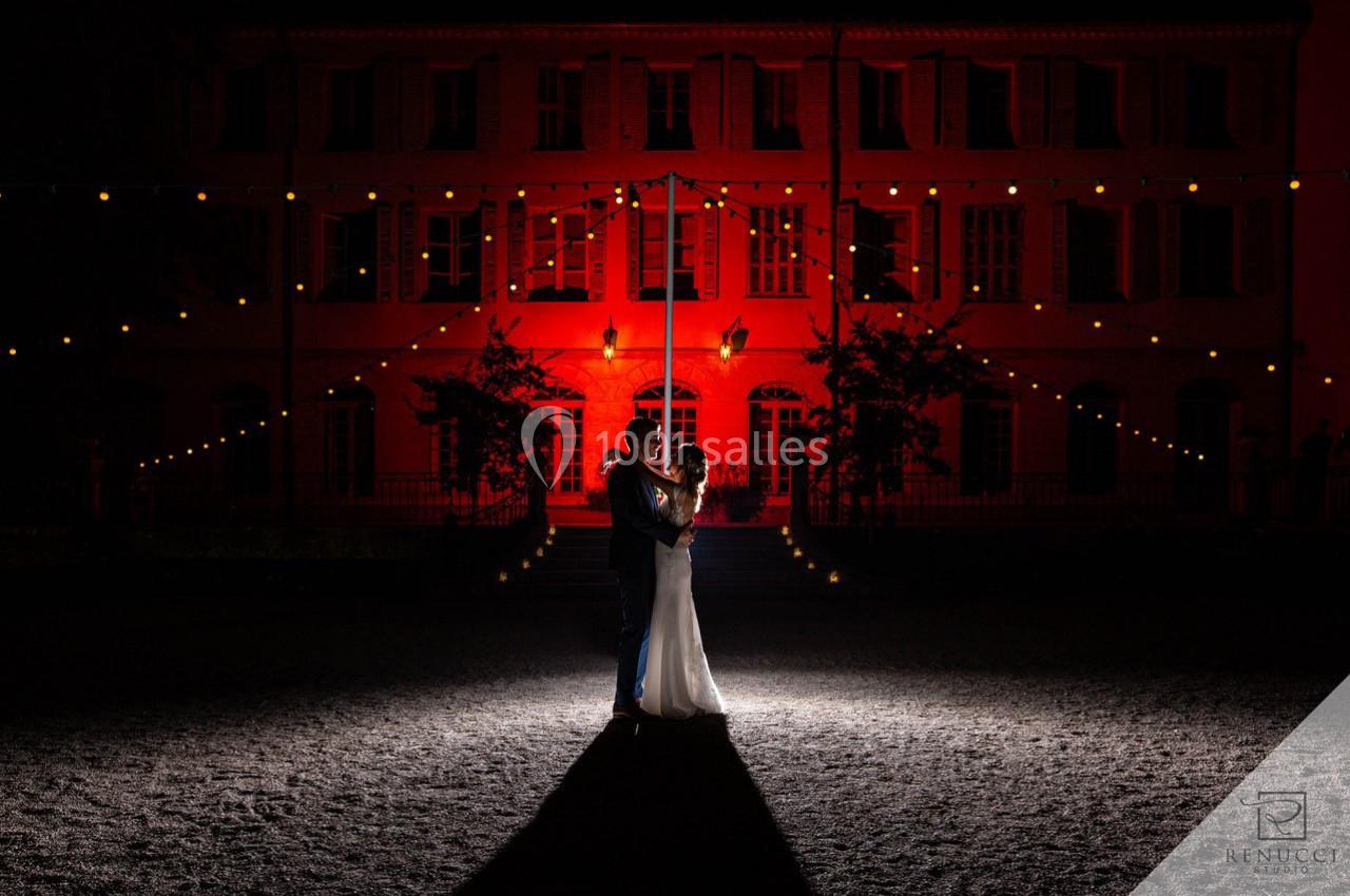 Un couple danse sous des guirlandes lumineuses devant un bâtiment éclairé en rouge, de nuit.