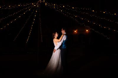 Un couple danse sous des guirlandes lumineuses devant un bâtiment éclairé en rouge, de nuit.