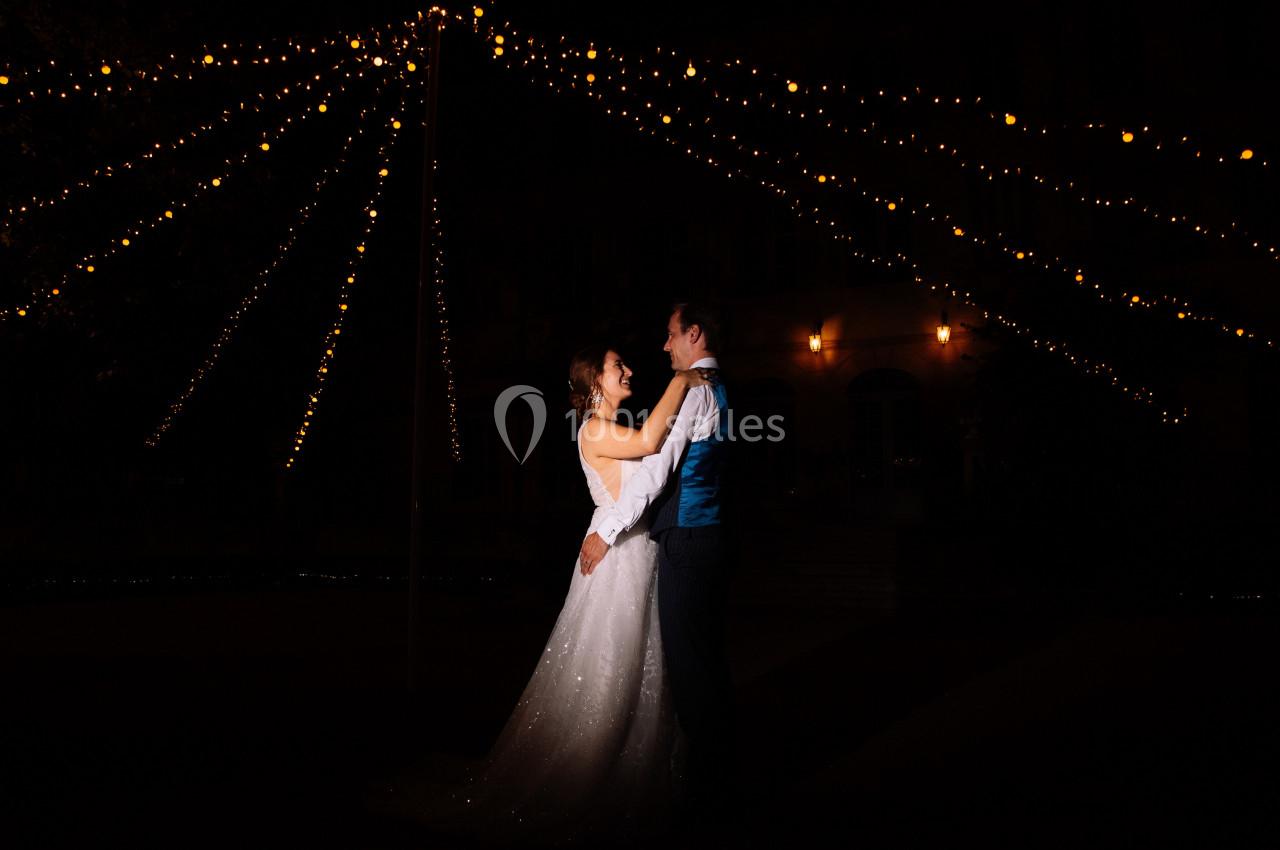 Un couple danse sous des guirlandes lumineuses dans un décor nocturne.