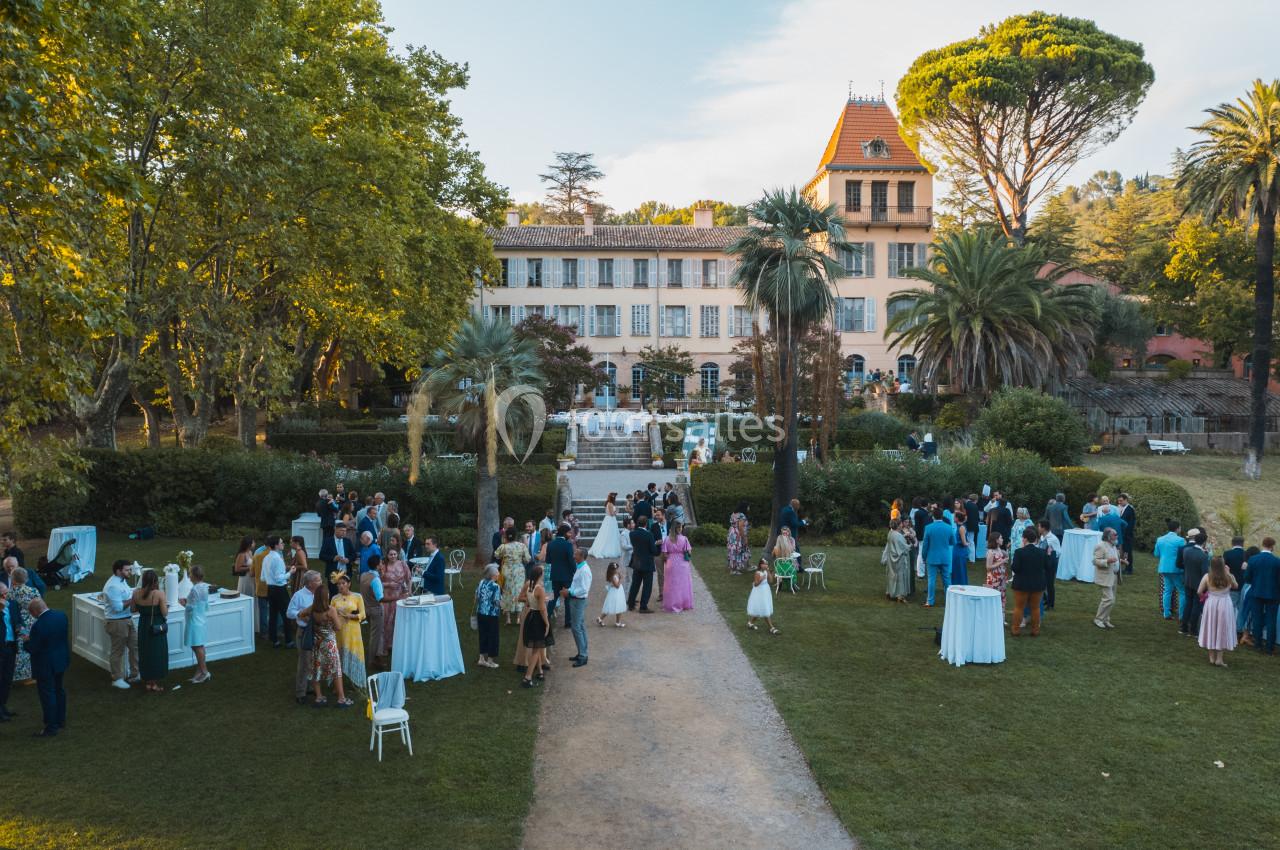 Groupe de personnes rassemblées dans un jardin devant un grand bâtiment historique entouré d'arbres.