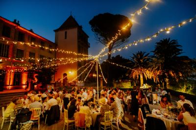 Un couple danse sous des guirlandes lumineuses devant un bâtiment éclairé en rouge, de nuit.